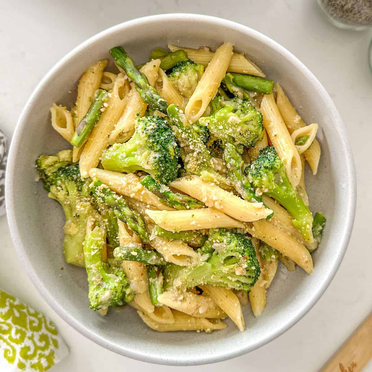 Bowl of pasta with asparagus and broccoli and vegan parmesan cheese on top.