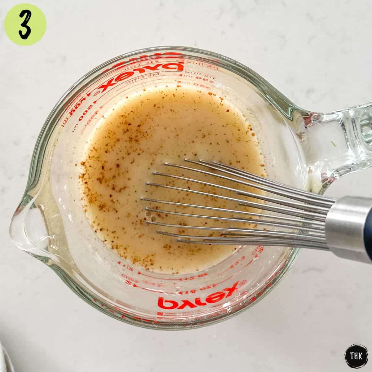 Milk, broth, seasoning and flour being whisked inside measuring cup.
