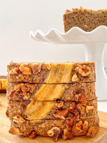 Four slices of banana bread stacked vertically on cutting board.