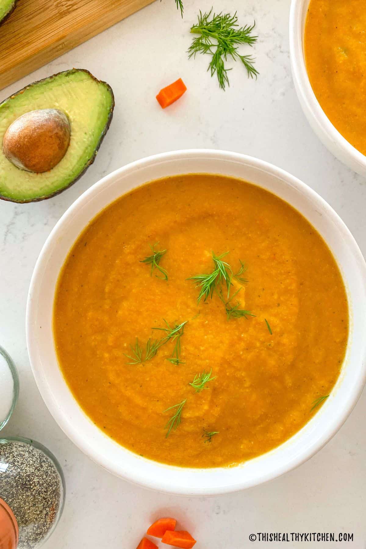 Bowl filled with orange soup with fresh dill on tpo.