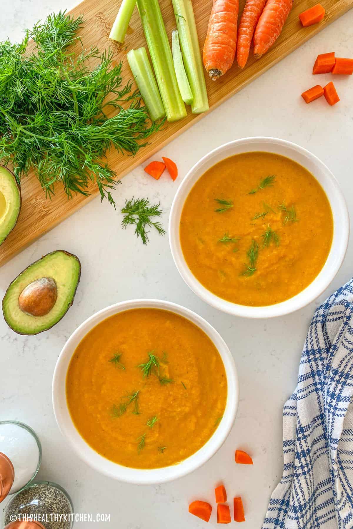 Two bowls of carrot soup on kitchen counter top.