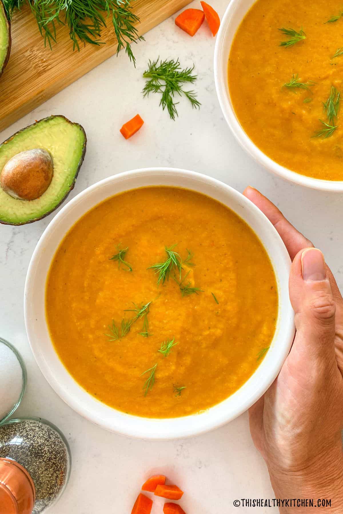 Bowl of carrot soup with hand holding the side of the bowl.
