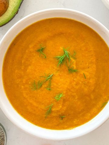 Bowl filled with orange soup with fresh dill on tpo.