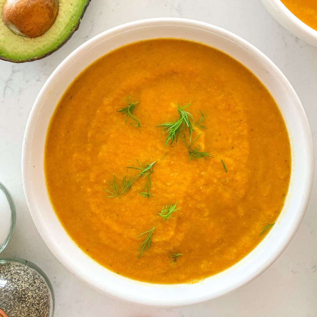 Bowl filled with orange soup with fresh dill on tpo.