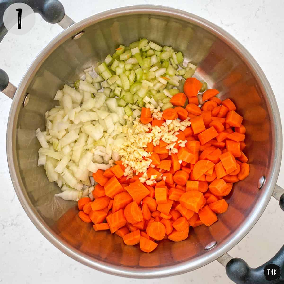 Soup pot with chopped onion, carrot, celery and garlic inside.