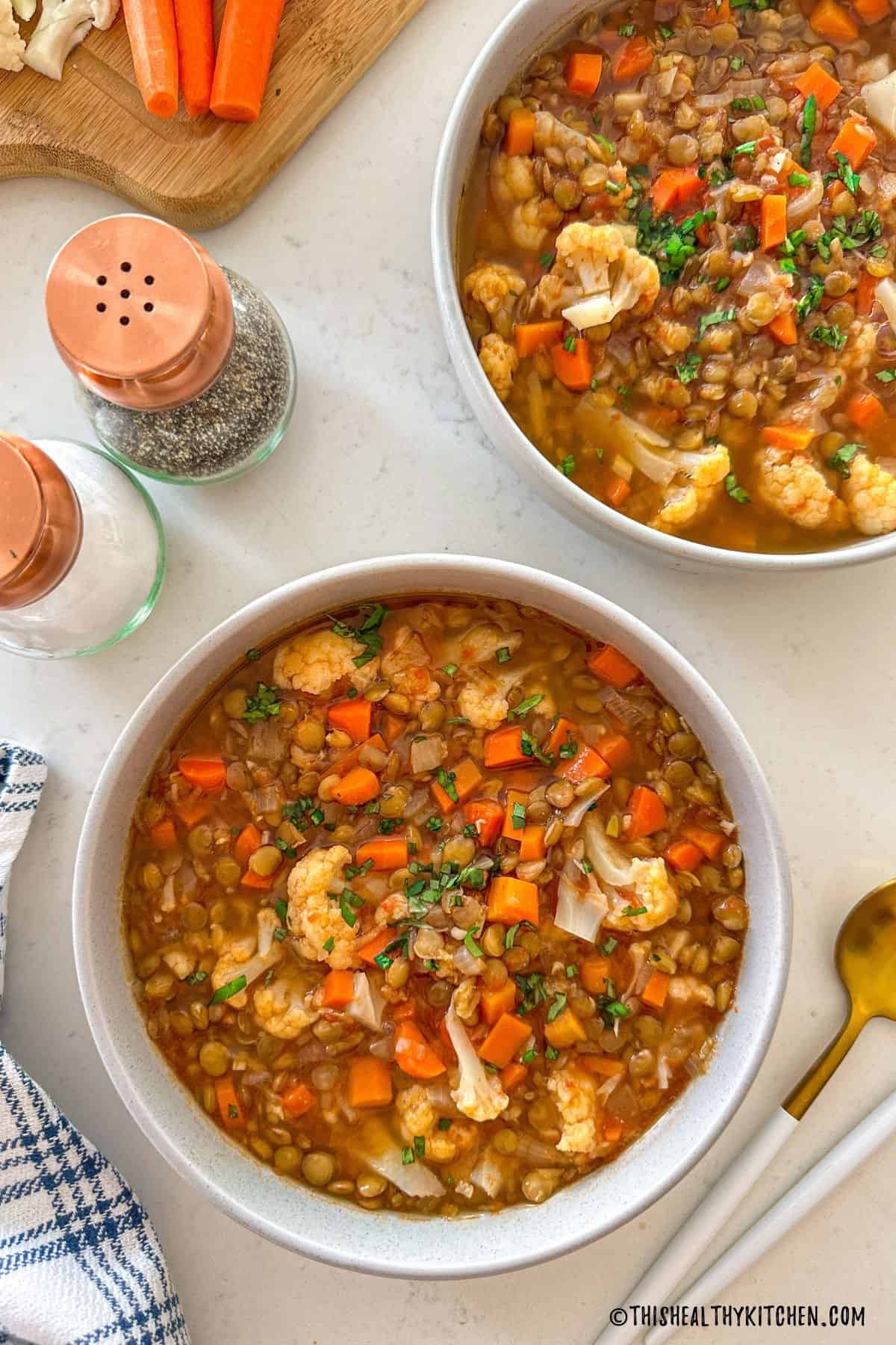 Two bowls of cauliflower and lentil soup with salt and pepper shaker beside them.