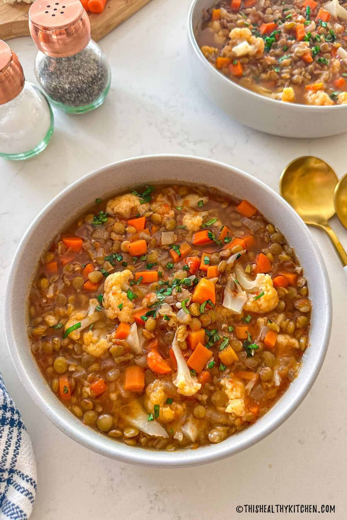Two bowls of cauliflower lentil soup with two gold spoons beside them.