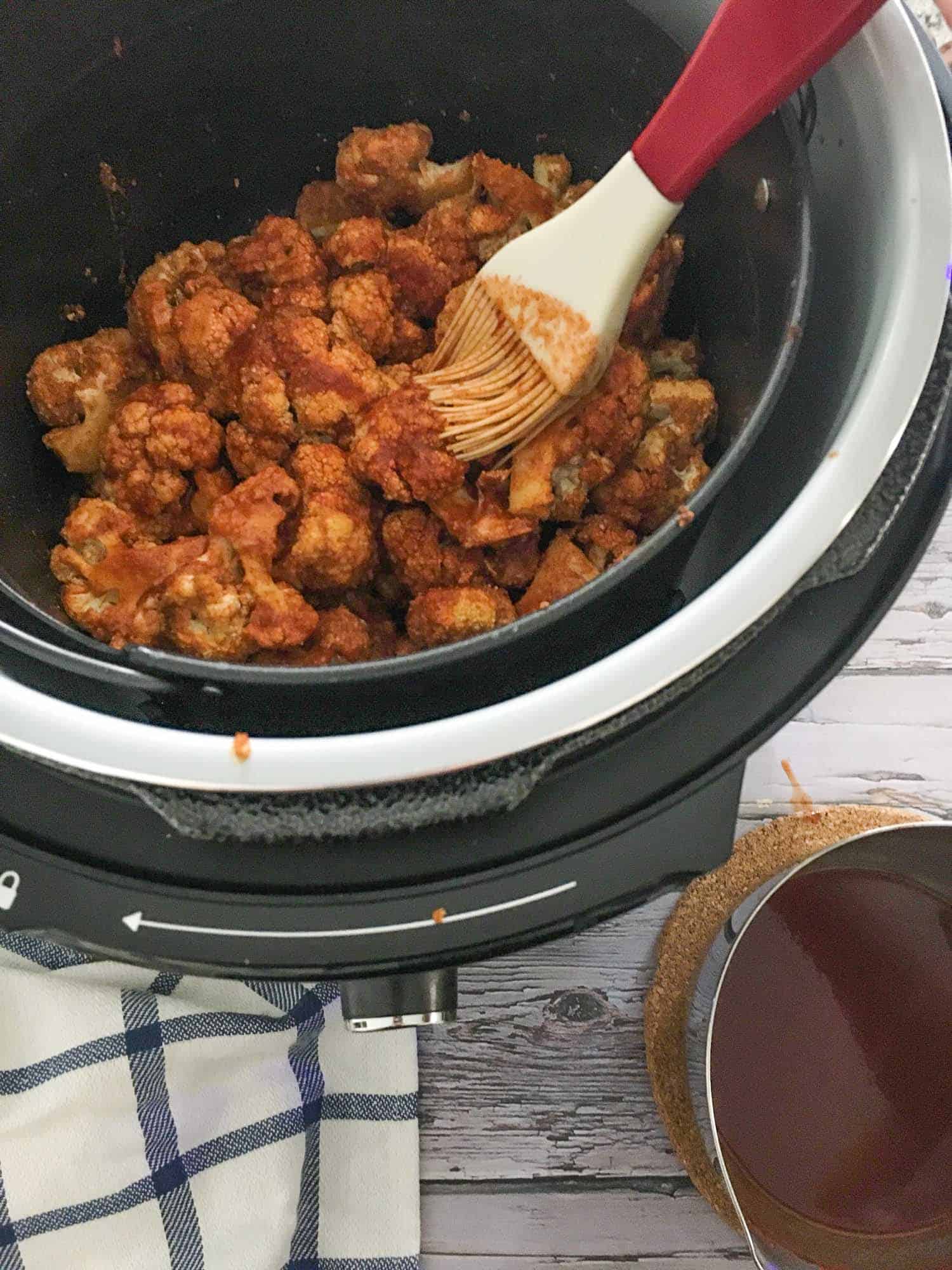 Brushing cauliflower florets with hot sauce using a silicone brush.