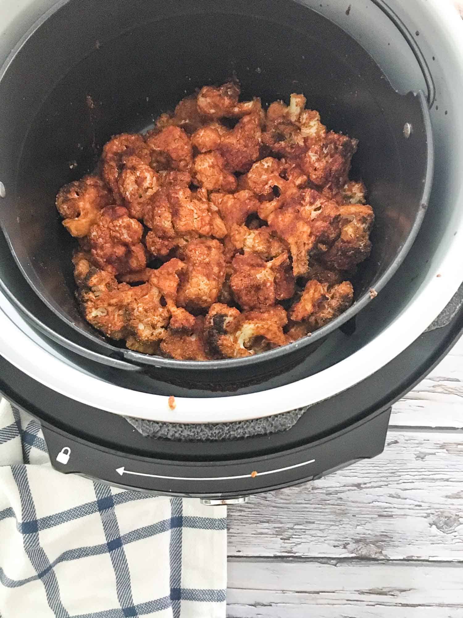 Cooked cauliflower florets that are red and covered in buffalo sauce inside air fryer basket.