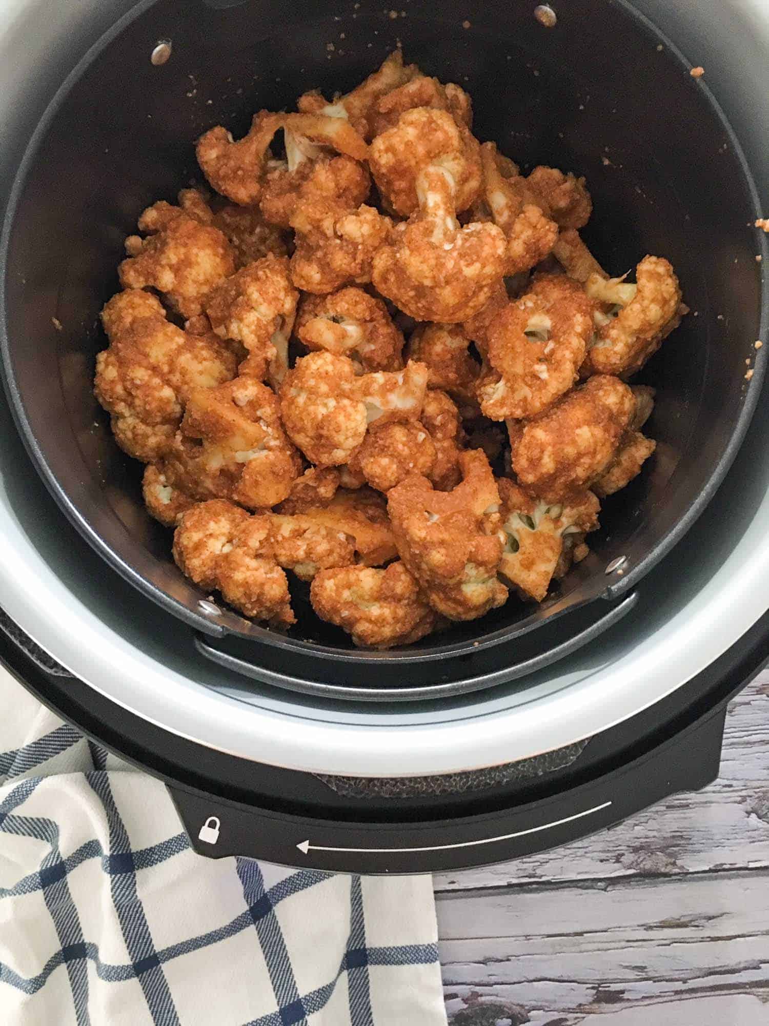 Cauliflower florets with hot sauce inside air fryer basket.
