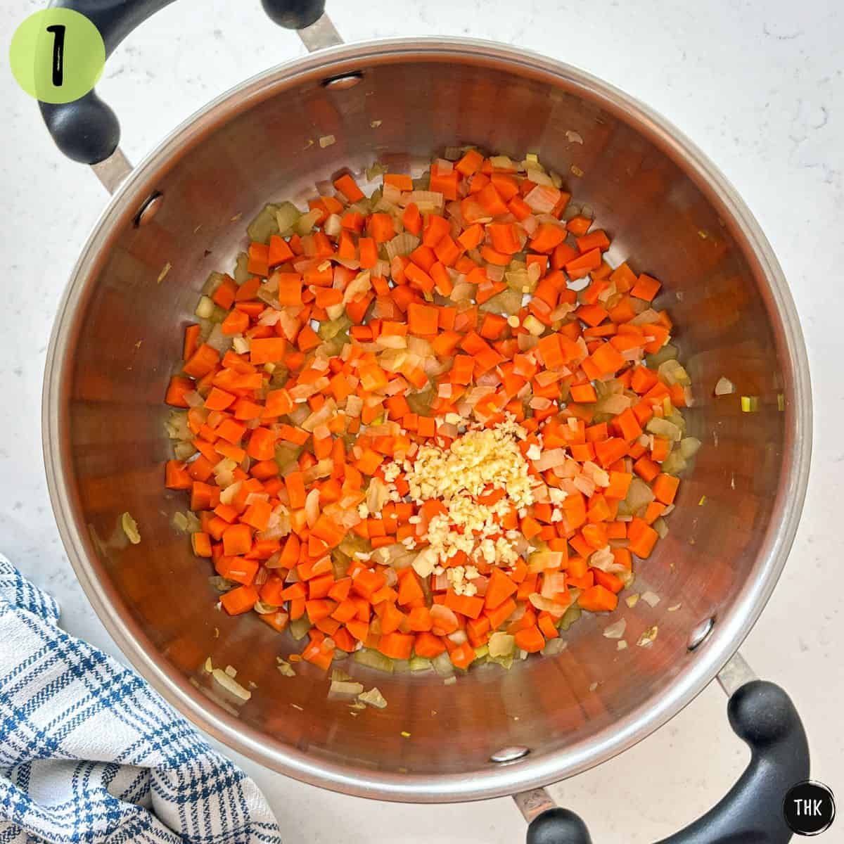 Pot with sauteed onions, carrots and minced garlic inside.