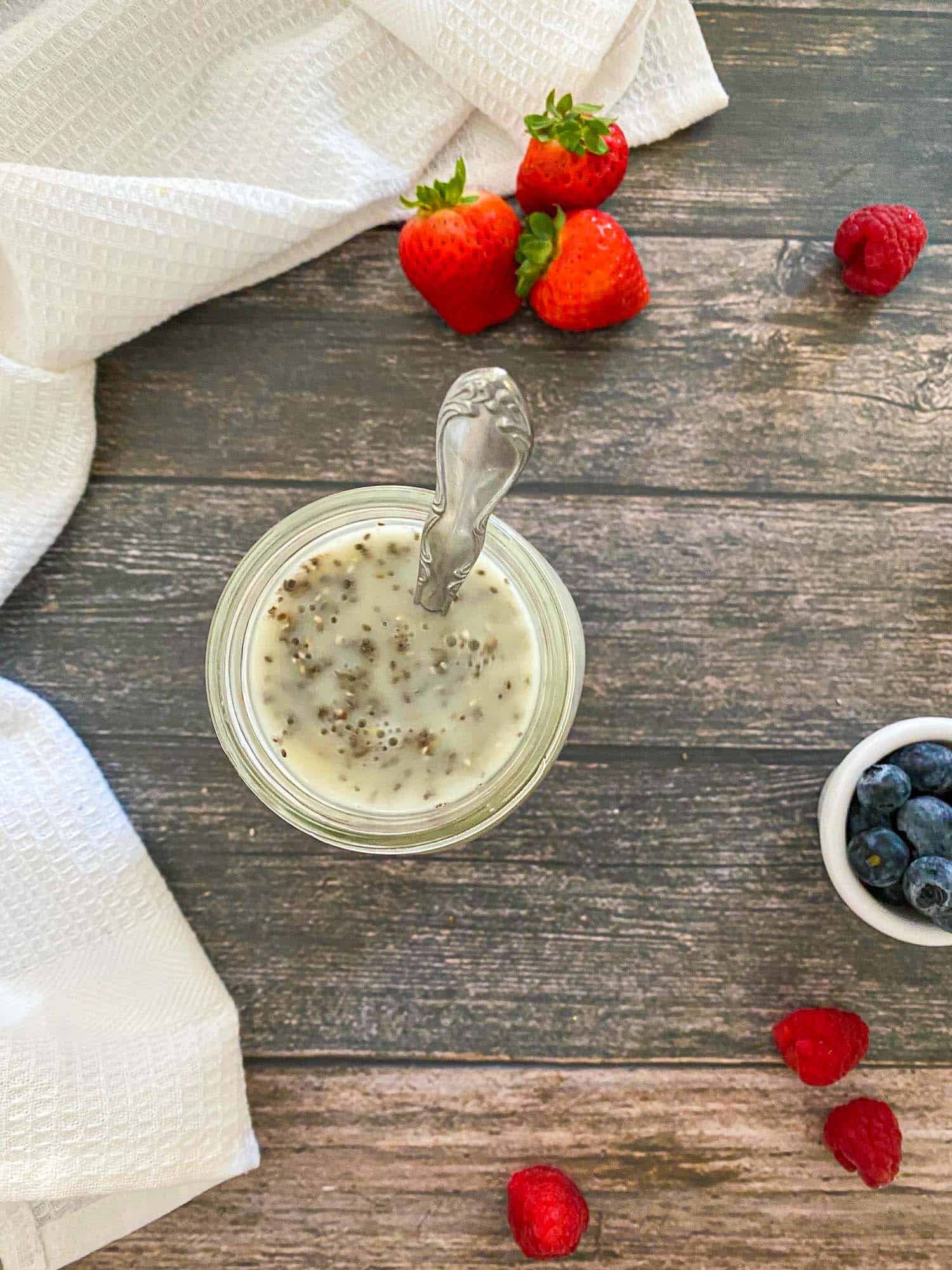 Milk and chia seeds stirred in glass jar with spoon inside.