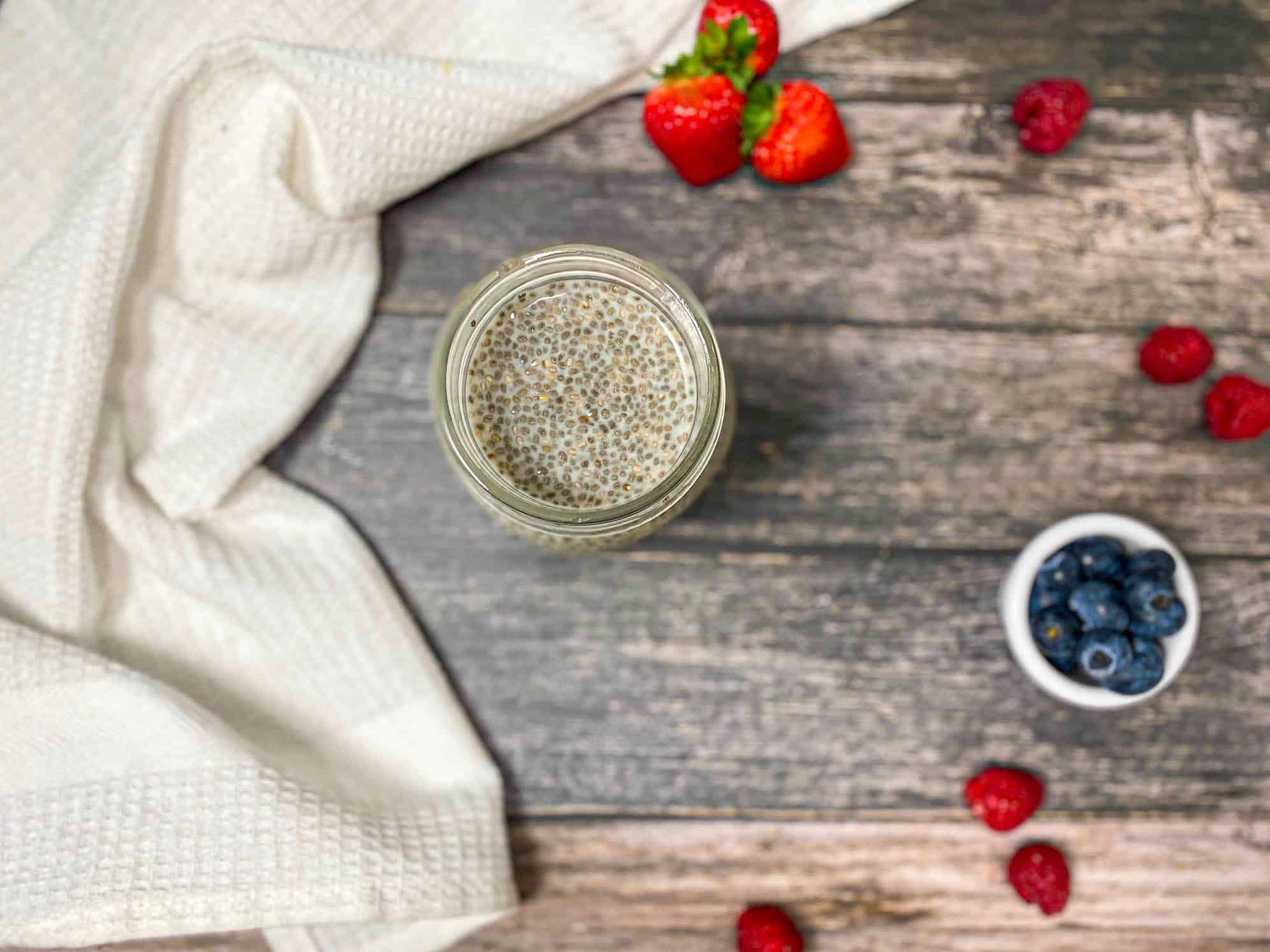 Over head view of glass jar with milk and chia seeds inside and berries around it.
