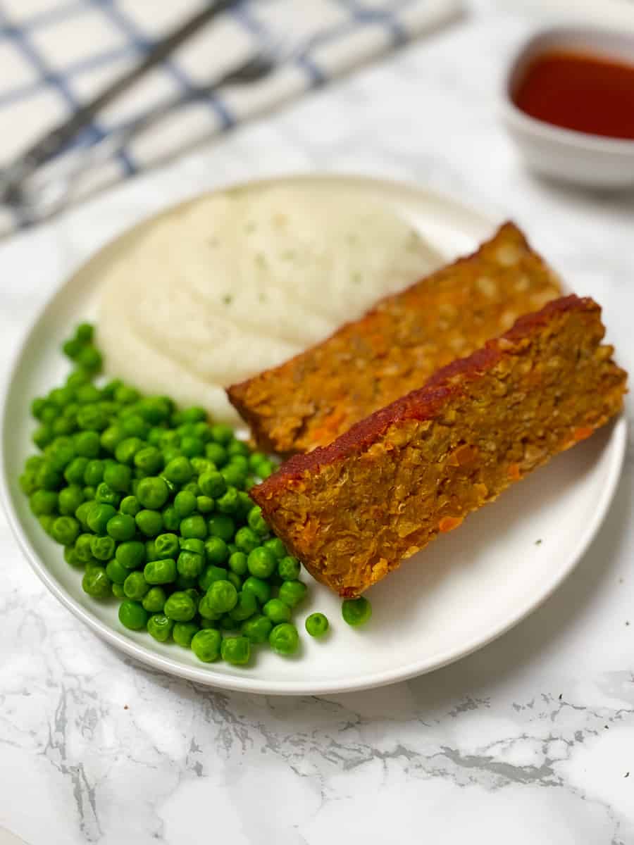 two slices of vegan loaf with mashed cauliflower and sweet peas on round plate