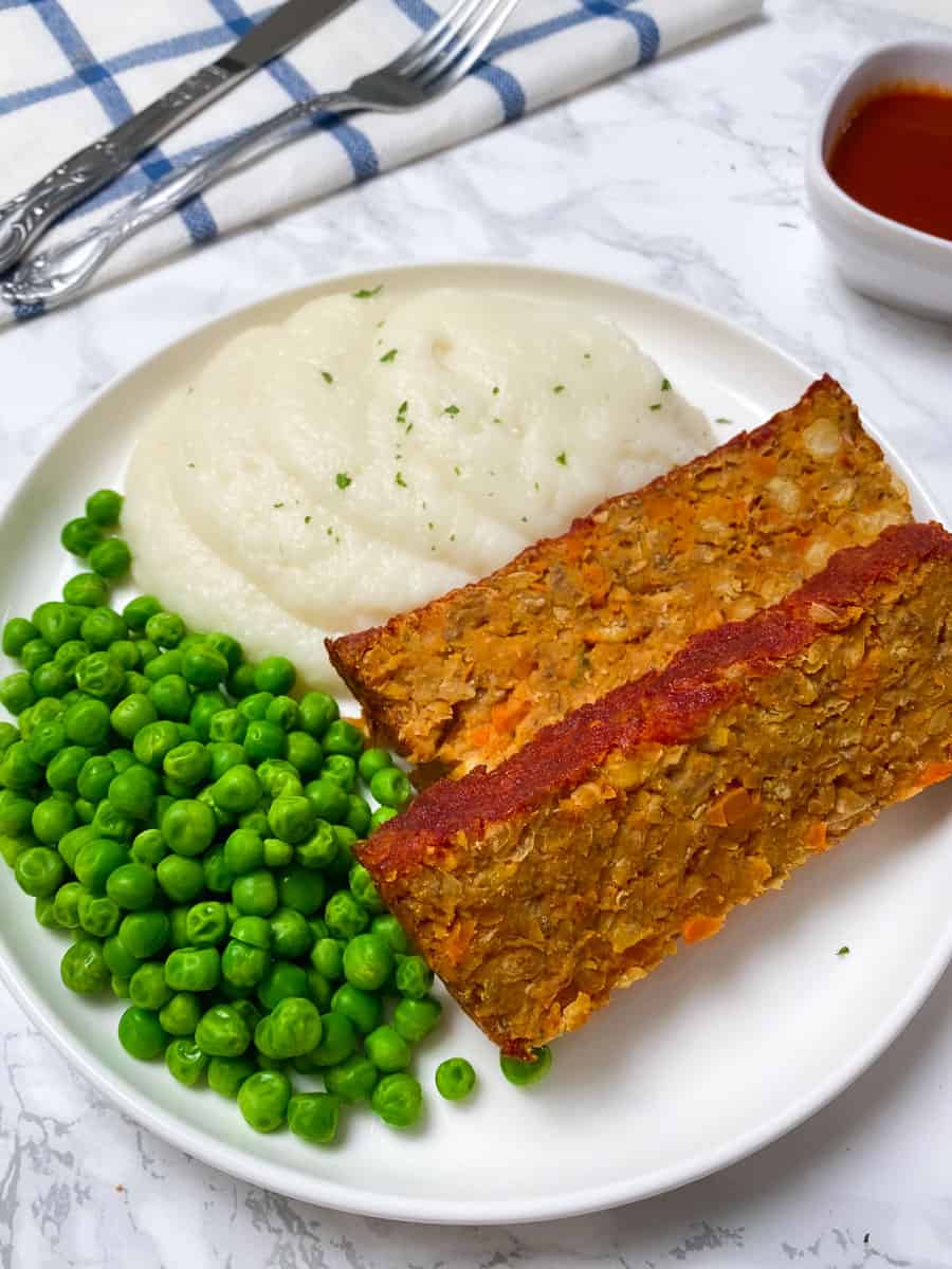 chickpea loaf on plate with side of mashed cauliflower and green peas