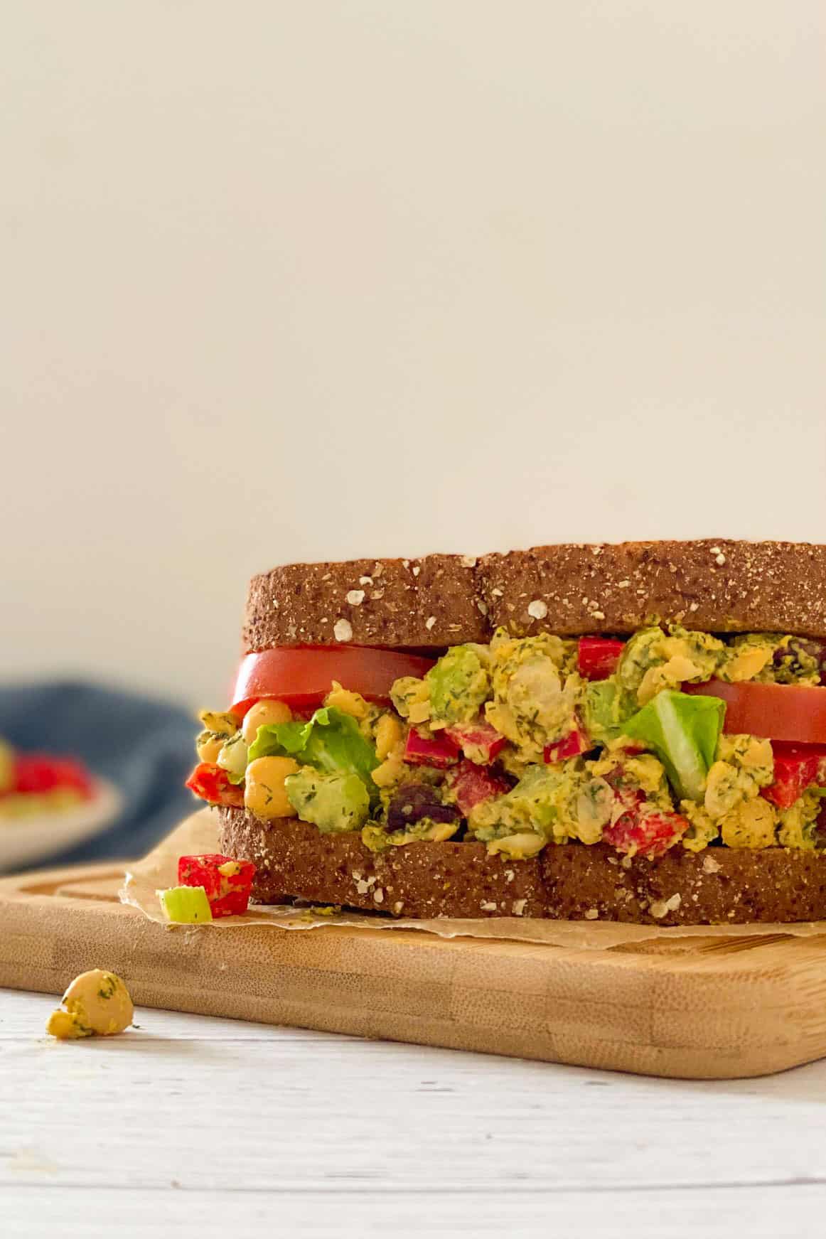Chickpea salad sandwich on cutting board with chickpeas and pepper falling out.