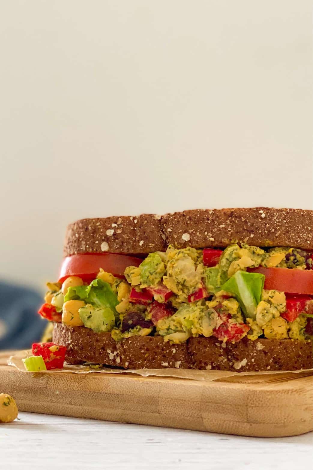 Sandwich resting on cutting board with chickpeas, tomato, celery, peppers and dill.