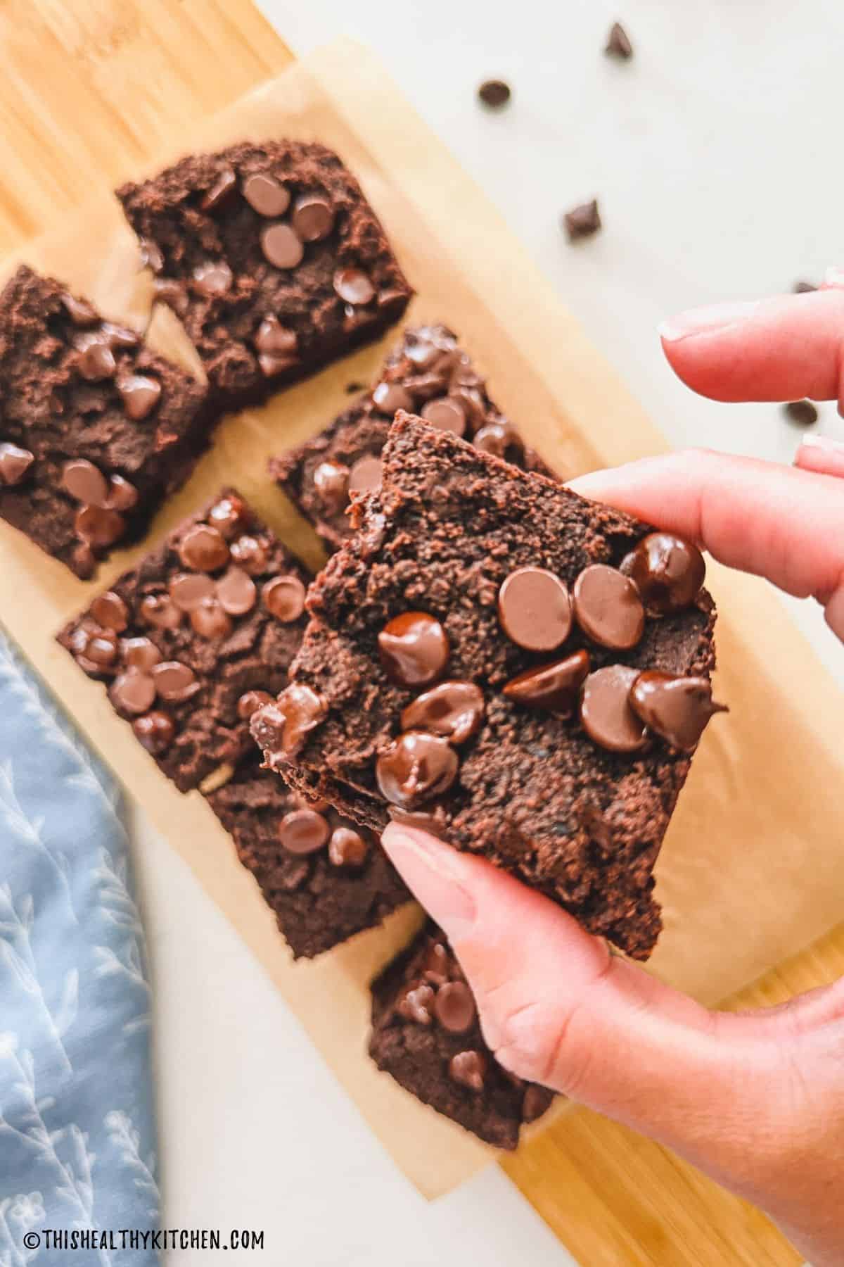 Hand holding up black bean chocolate cake slice with more slices on cutting board below.