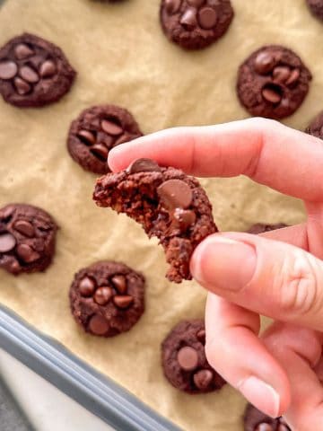 Hand holding a chocolate chickpea cookie with bite taken out.