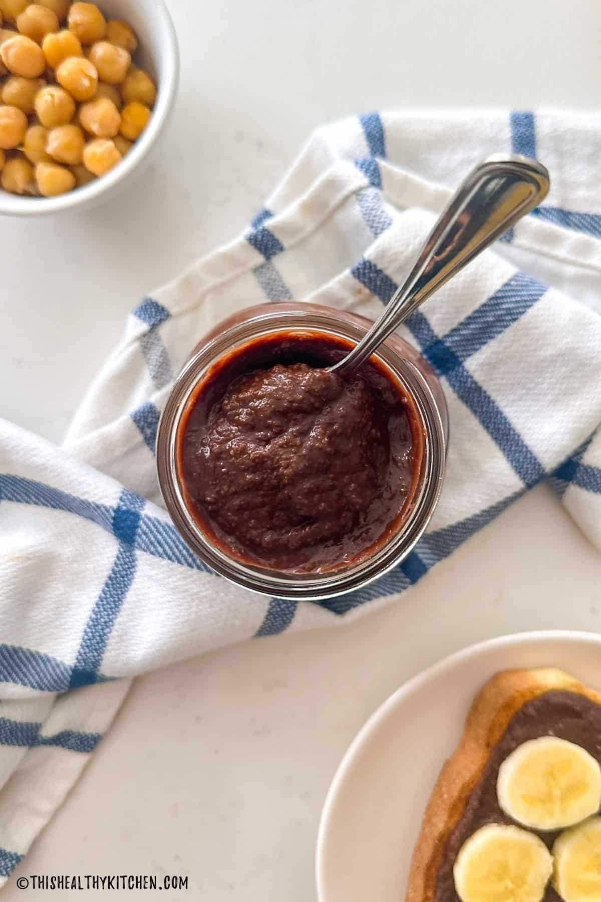 Jar of nut-free nutella with spoon inside it and bowl of chickpeas beside it.