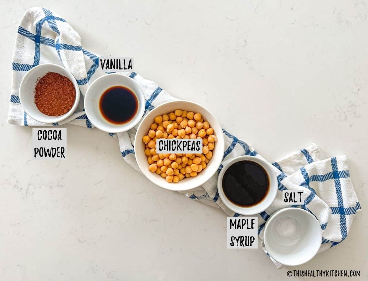 Bowls of chickpeas, cocoa powder, vanilla, maple syrup, and salt on countertop.
