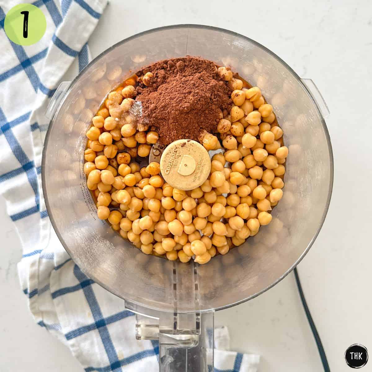 Food processor bowl with chickpeas, raw cocoa and maple syrup inside.