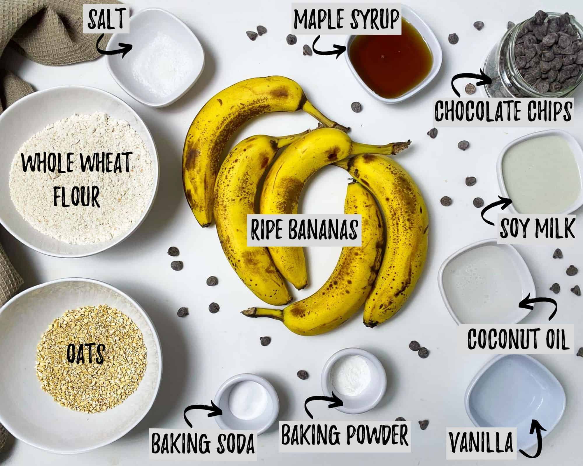 bananas, bowl of flour, bowl of oats, baking powder, baking soda, maple syrup, vanilla, milk, oil, salt