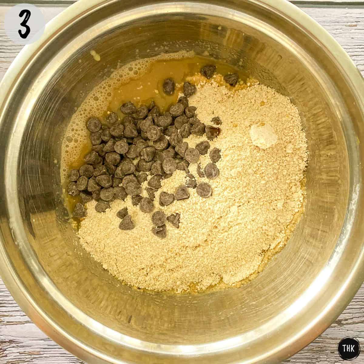 Mixing bowl with wet and dry ingredients and chocolate chips on top.