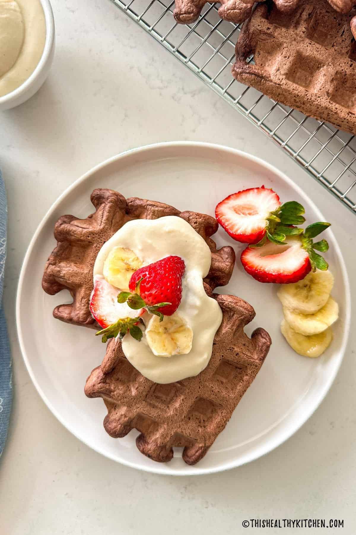 Two chocolate waffles on plate with vegan whipped cream, strawberries and banana on top.