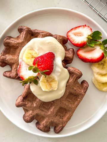 Two chocolate waffles on plate with vegan whipped cream, strawberries and banana on top.