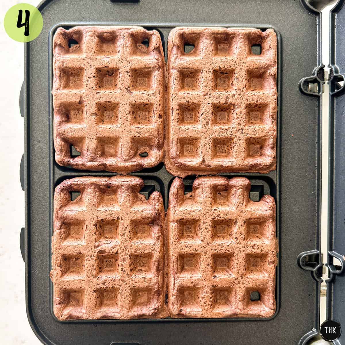 Four chocolate waffles cooking on waffle iron.