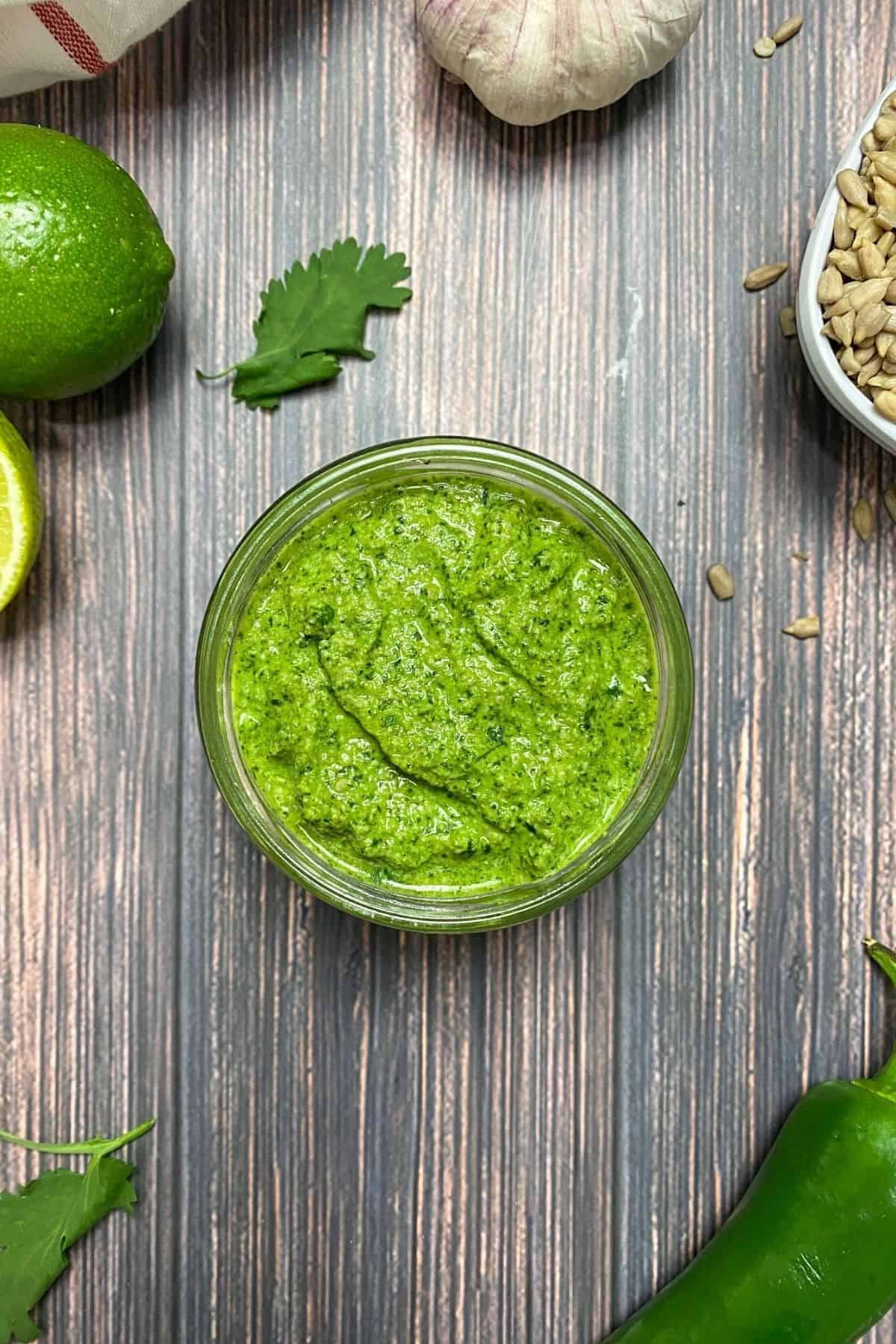 Open jar of pesto sauce with lime, garlic and cilantro in background.