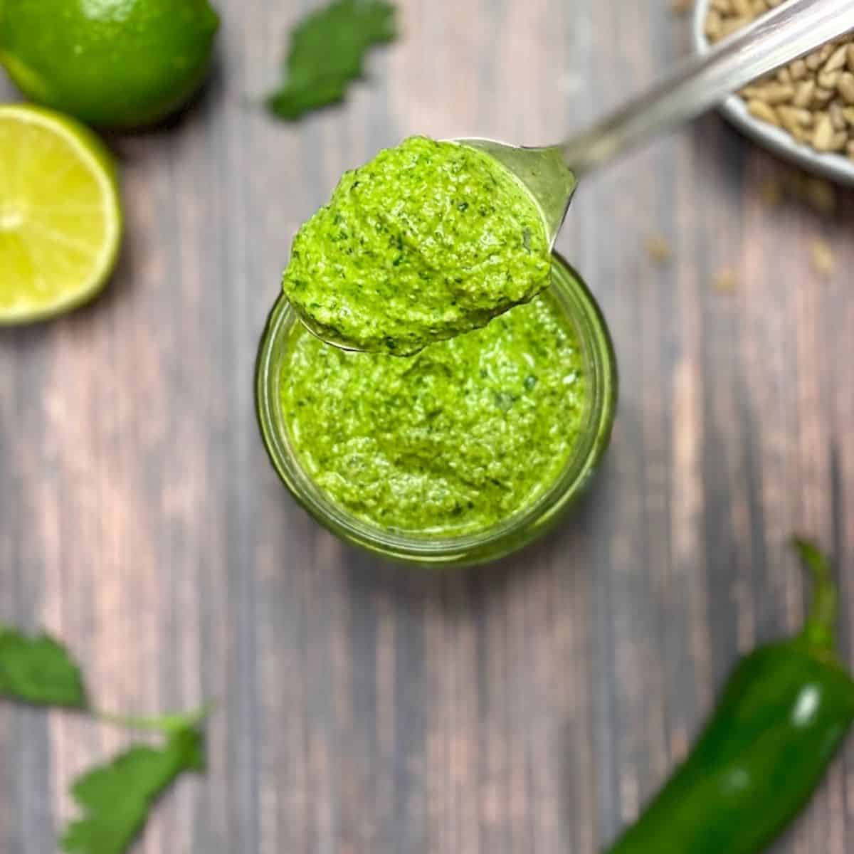 Cilantro pesto in glass jar with lime, sunflower seeds and jalapeno in the background