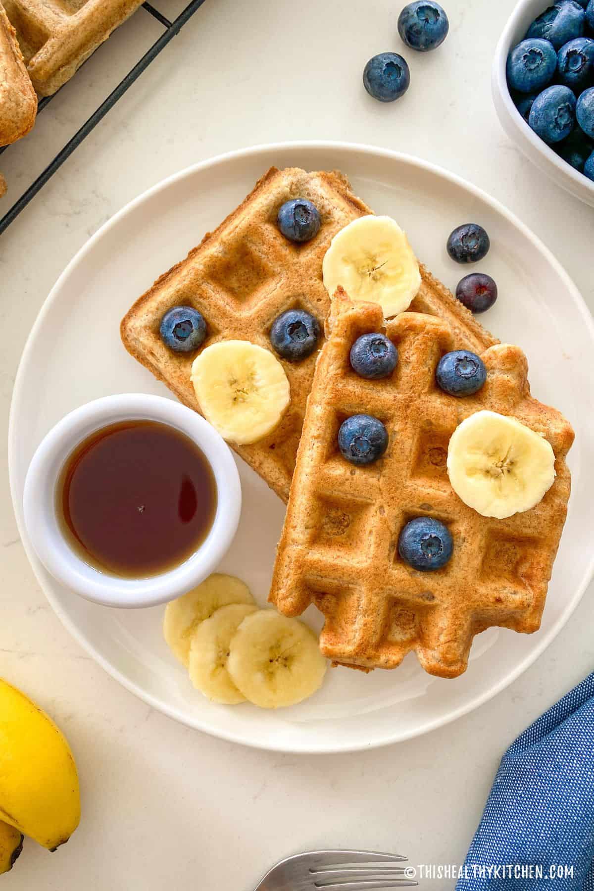 Plate with two waffles, with banana slices and blueberries on top.