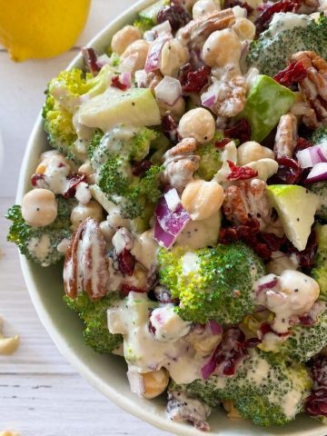 Large salad in white serving bowl with lemons, pecans, and cranberries around it.