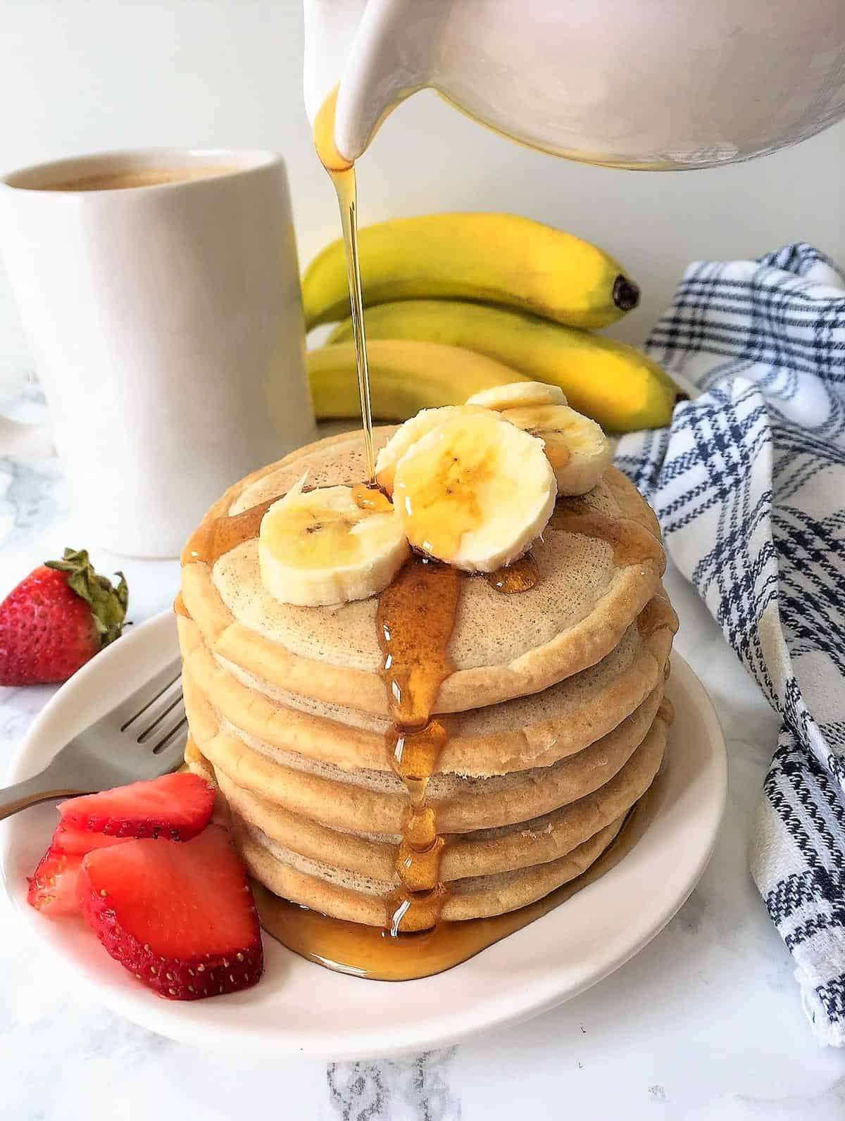 Stack of pancakes on plate with banana and strawberry slices.