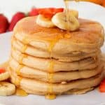 stack of vegan pancakes with banana slices on top and syrup dripping down.