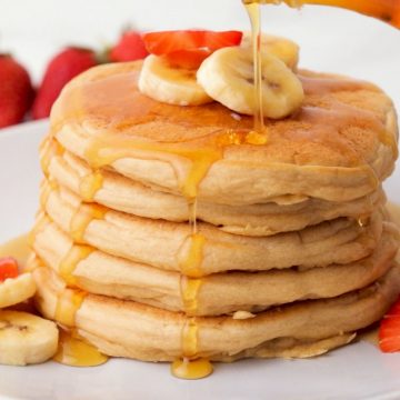 stack of vegan pancakes with banana slices on top and syrup dripping down.
