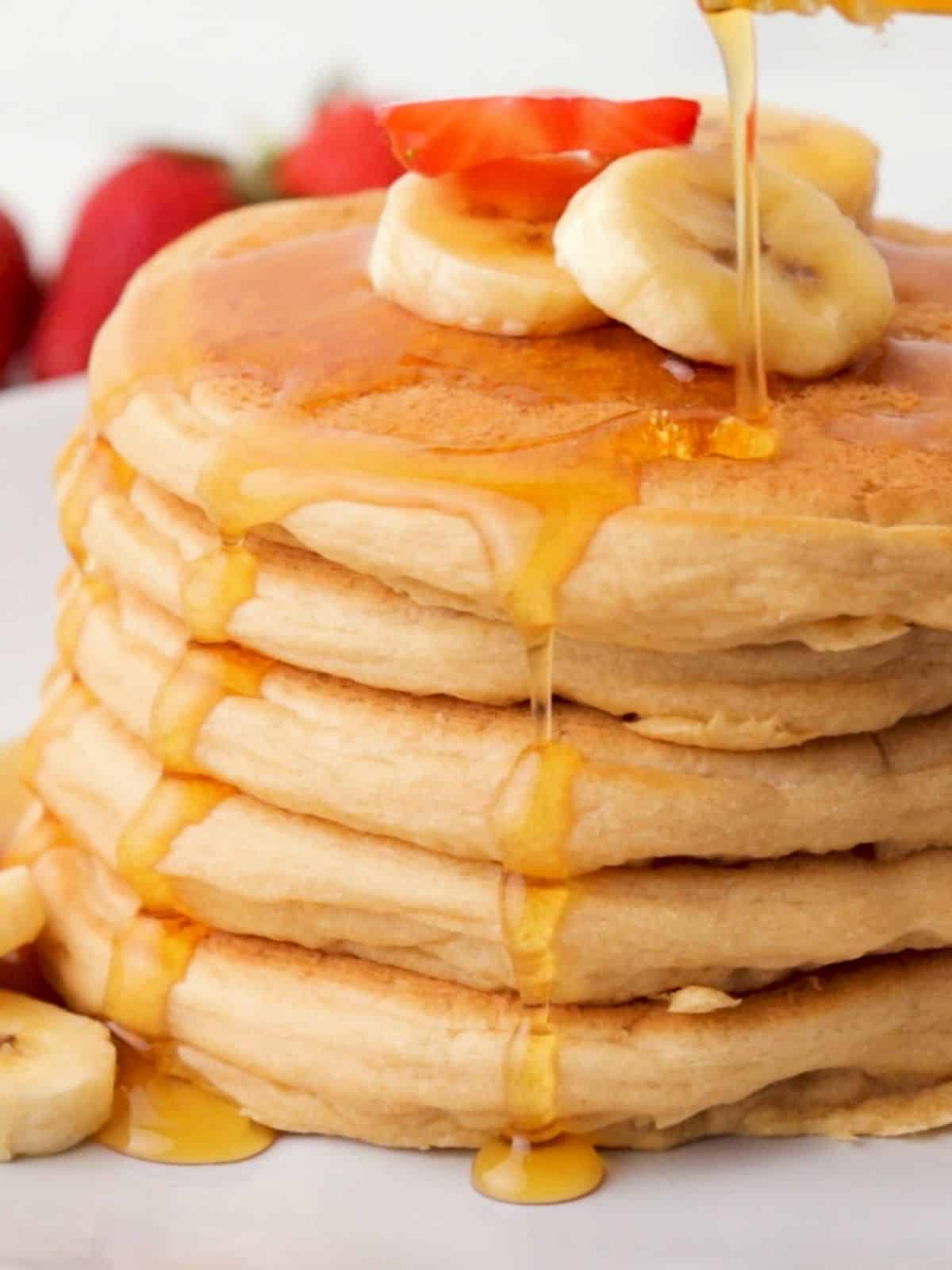 stack of vegan pancakes with banana slices on top and syrup dripping down.
