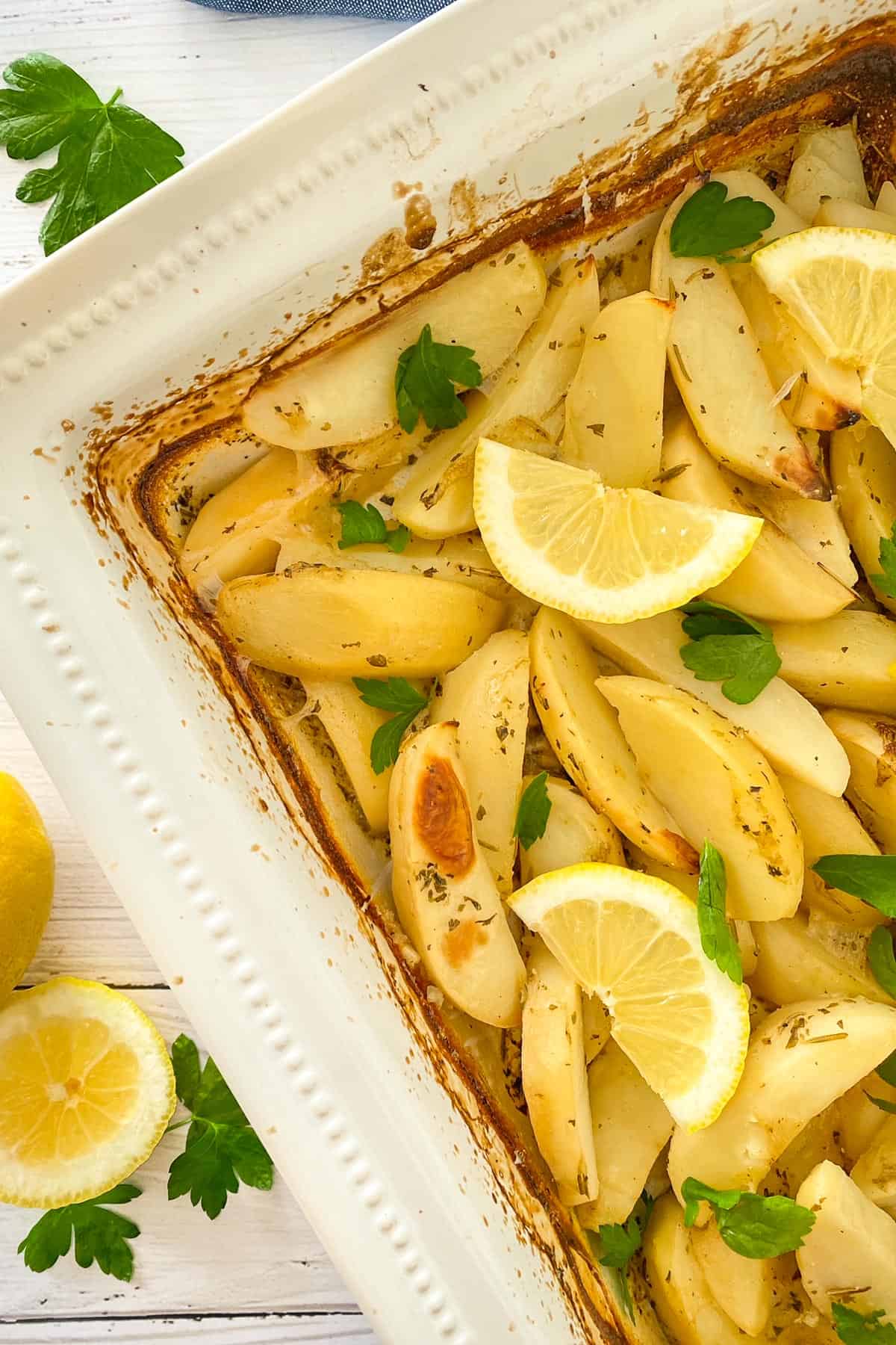 Roasted potatoes in white tray with lemon wedges and parsley garnish.