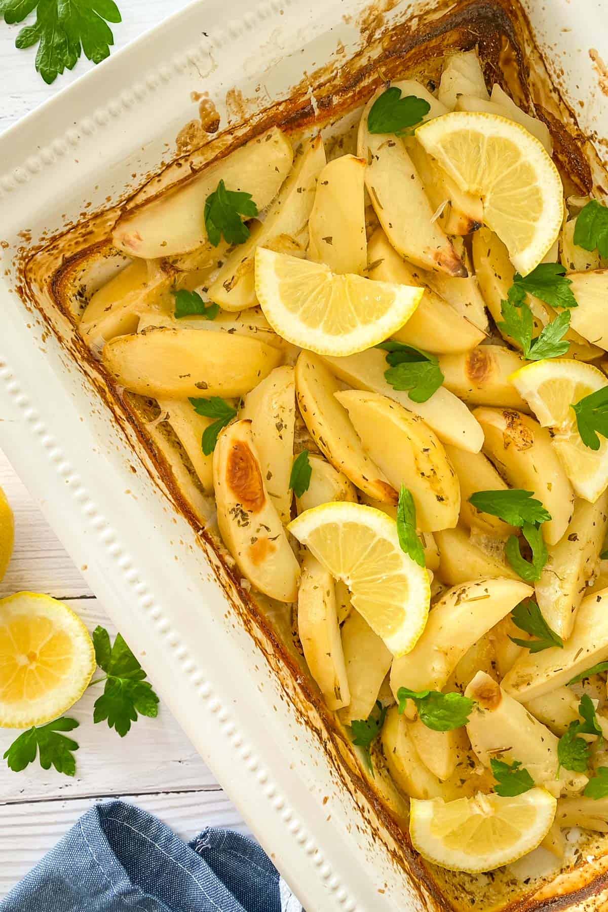 White baking dish filled with roasted potatoes with lemon wedges and parsley on top.