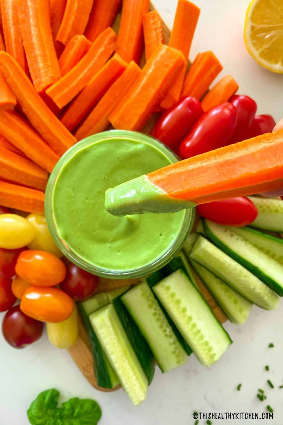 Carrot stick being dipped into green sauce.