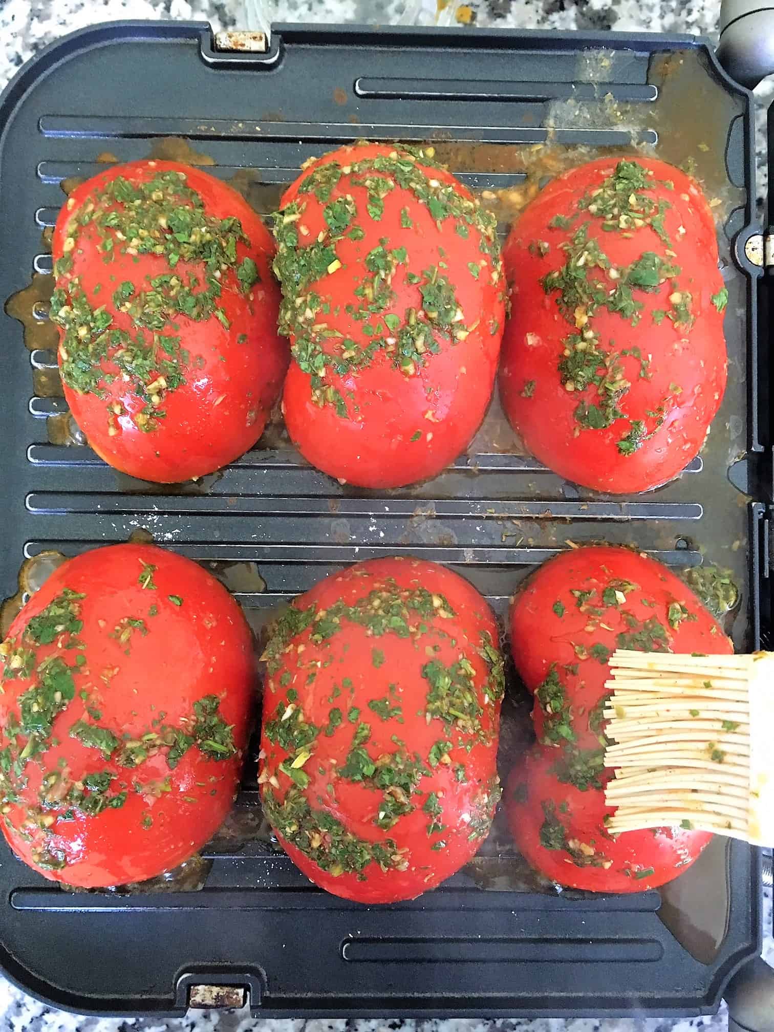 Halved tomatoes on grill being brushed with chimichurri sauce.