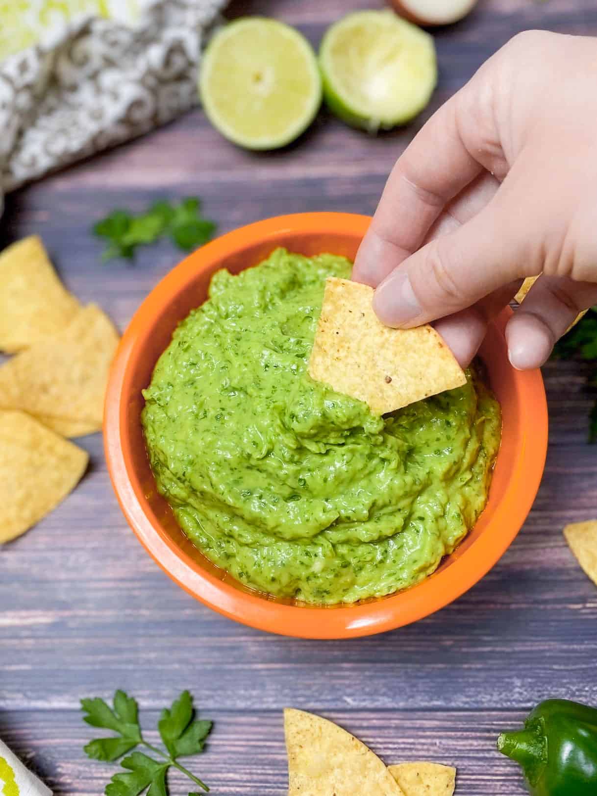 dipping tortilla chip into green dip