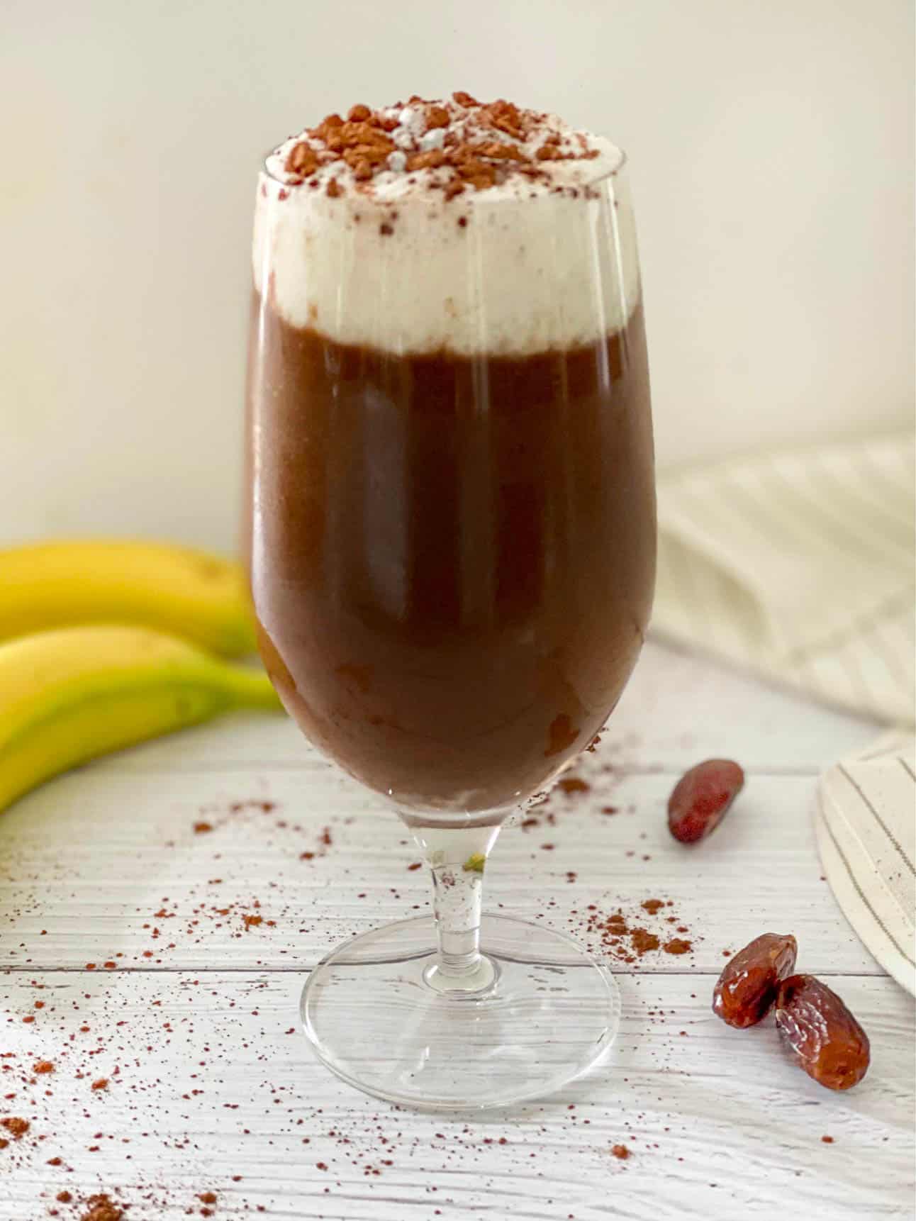 Clear glass with chocolate drink and frothed milk on top with sprinkle of cinnamon.