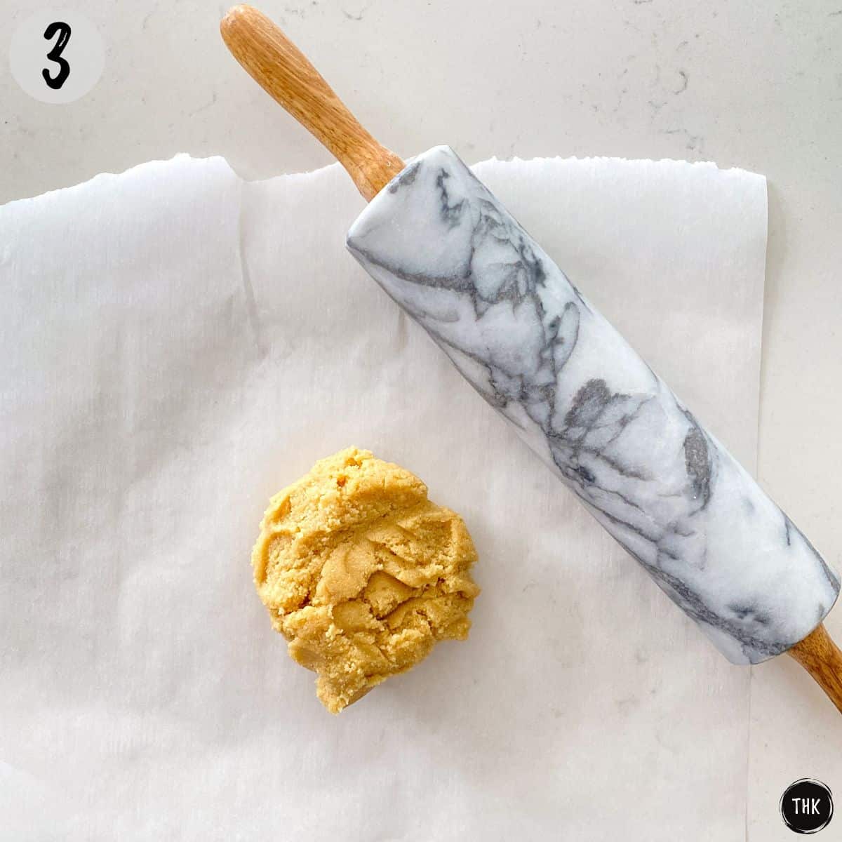 Ball of dough on parchment paper with rolling pin beside it.