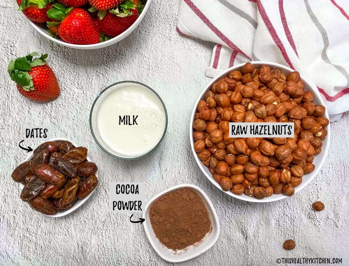 Bowl of hazelnuts, dates, strawberries, cocoa powder and glass of milk.