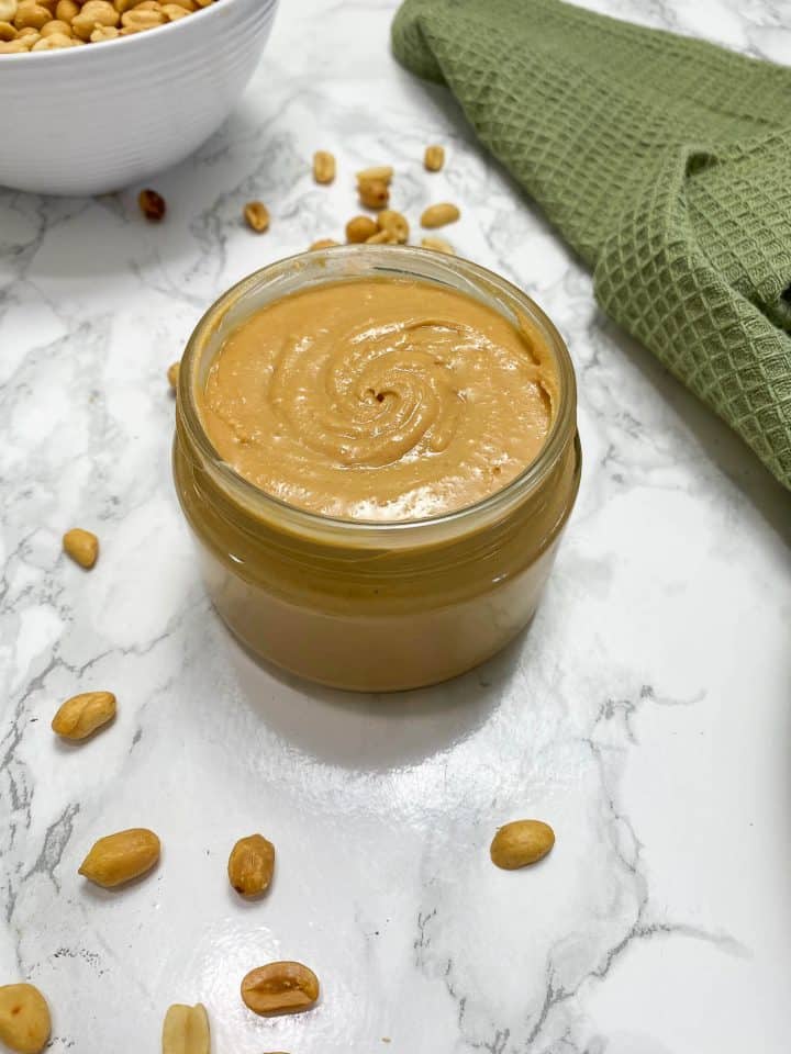 peanut butter in jar with peanuts and green towel around it