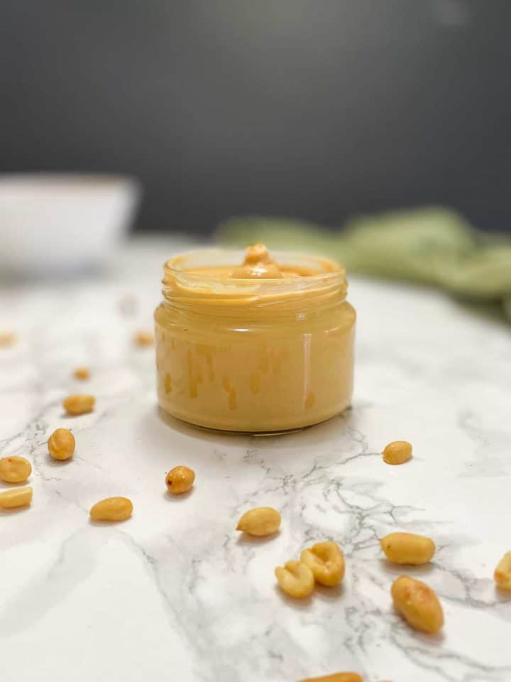 peanut butter in glass jar with peanuts scattered around the jar