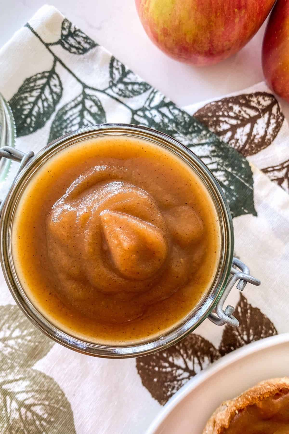 Glass jar filled with homemade apple butter with apples in the background.